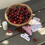 Big Effing Clip in Cherry Gingham assorted hair claw clips, hair care, playing cards, and cherries in a basket.