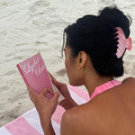 Big Effing Clip in Lychee Baby closeup of model wearing Big Effing Clip in Lychee Baby while reading book and laying on towel at beach