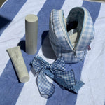 Bow Barrette in Baby Blue Gingham Bow Barrette in Baby Blue Gingham with pouch and hair care on striped towel
