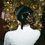 Iconic Velvet Bow Barrette in Noir model standing in front of Christmas tree wearing Bow Barrette in Iconic Velvet in hair