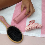 Flat Brush in Lychee Baby model holding aura hair + body mist in lychee baby next to claw clip and hair brush