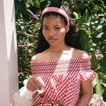 Halo Headband in Cherry Gingham model holding cherry while standing with Halo Headband in Cherry Gingham in hair