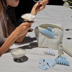 Popstar Clips in Blue Mist Eyelet model eating ice cream on table with assorted emi jay hair care, accessories, and pouch