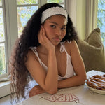 Ruffle Headband in Daffodil model with hand on cheek and Ruffle Headband in Daffodil in hair sitting at table in front of playing cards and apple pie