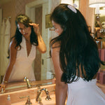 Sweetheart Clip in Angel Dust model looking in mirror while wearing Sweetheart Clip in Angel Dust with Halo Hair Oil on counter next to sink