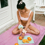 Big Effing Clip in Lilac Buttercream model cutting oranges while wearing Big Effing Clip in Lilac Buttercream + Terry Cloth Scrunchies in Sea Salt + Beach Berry + Sunkissed + Bikini
