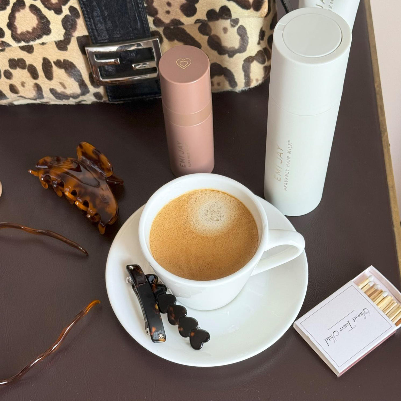 Assorted Emi Jay hair care, accessories, and matches with coffee and purse on table.