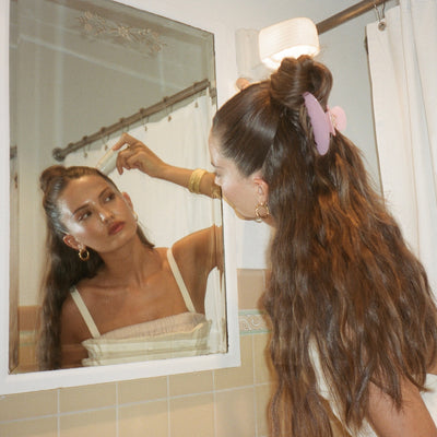 model applying angelstick to hair looking in the mirror while wearing Big Effing Clip in Cherub Pink