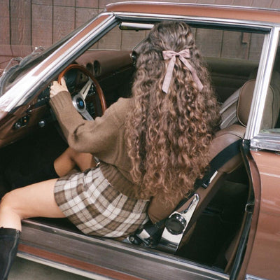 Model sitting in car wearing bow barrette in fireside.