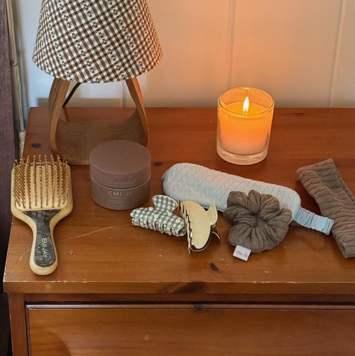 assorted emi jay hair care and accessories on side table with candle and lamp