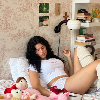 model laying in bed wearing EJ Lady Baby Tee