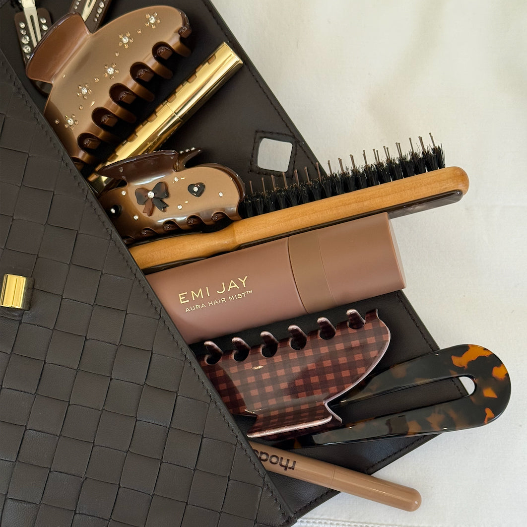 Assorted Emi Jay hair care, accessories, and styling tools in purse.