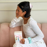 model sitting on pink couch wearing big effing clip and holding gift set with scrunchie on wrist