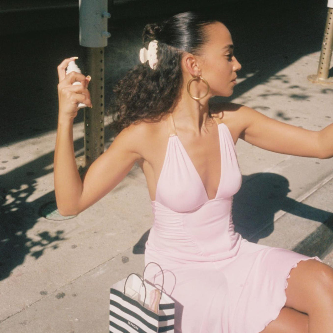 model spraying aura mist in hair while sitting on sidewalk with sweetheart clip in hair