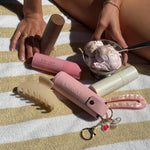 Aura Hair + Body Mist™ Keychain with aura hair + body mists, hair pin, and big effing clip next to bowl of ice cream and model on yellow and white striped towel