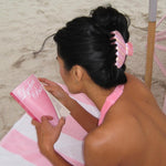model reading book while laying on towel at beach with Big Effing Clip in Lychee Baby in hair