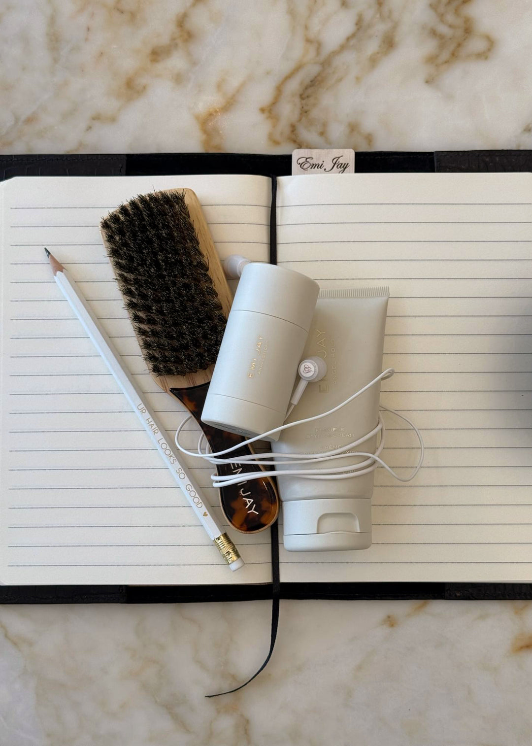 mini boar bristle brush, angelstick, angel hold, emi jay pencil, and headphones on book sitting on marble