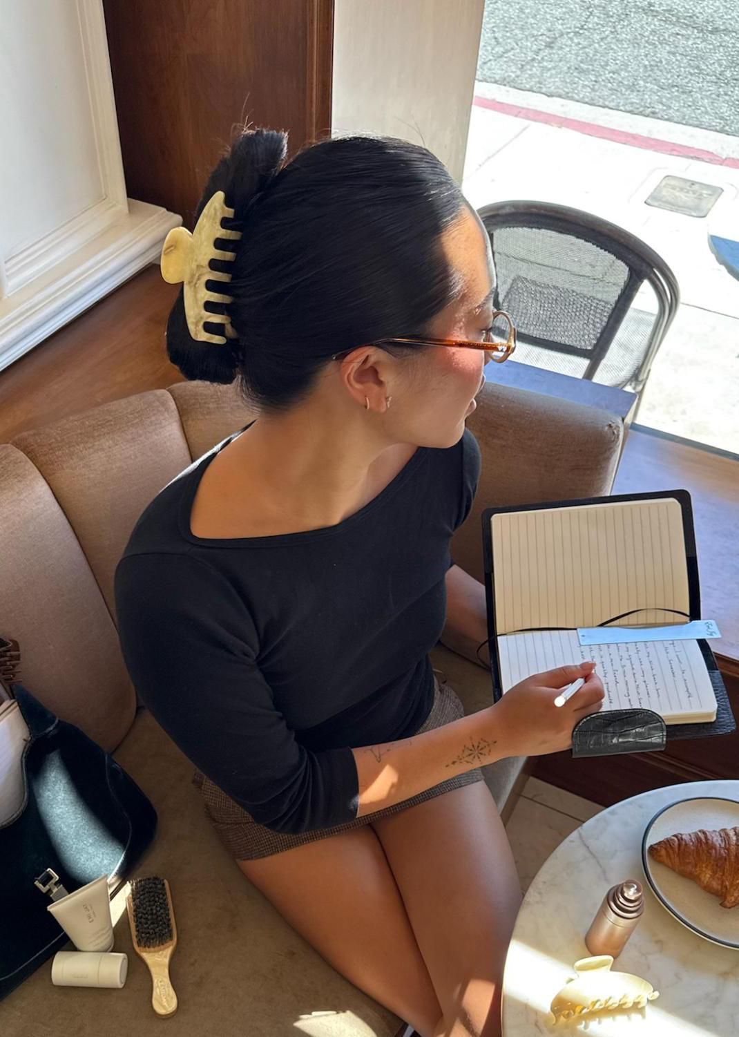 model wearing big effing clip while sitting at table with pastries, hair care, and accessories writing in book