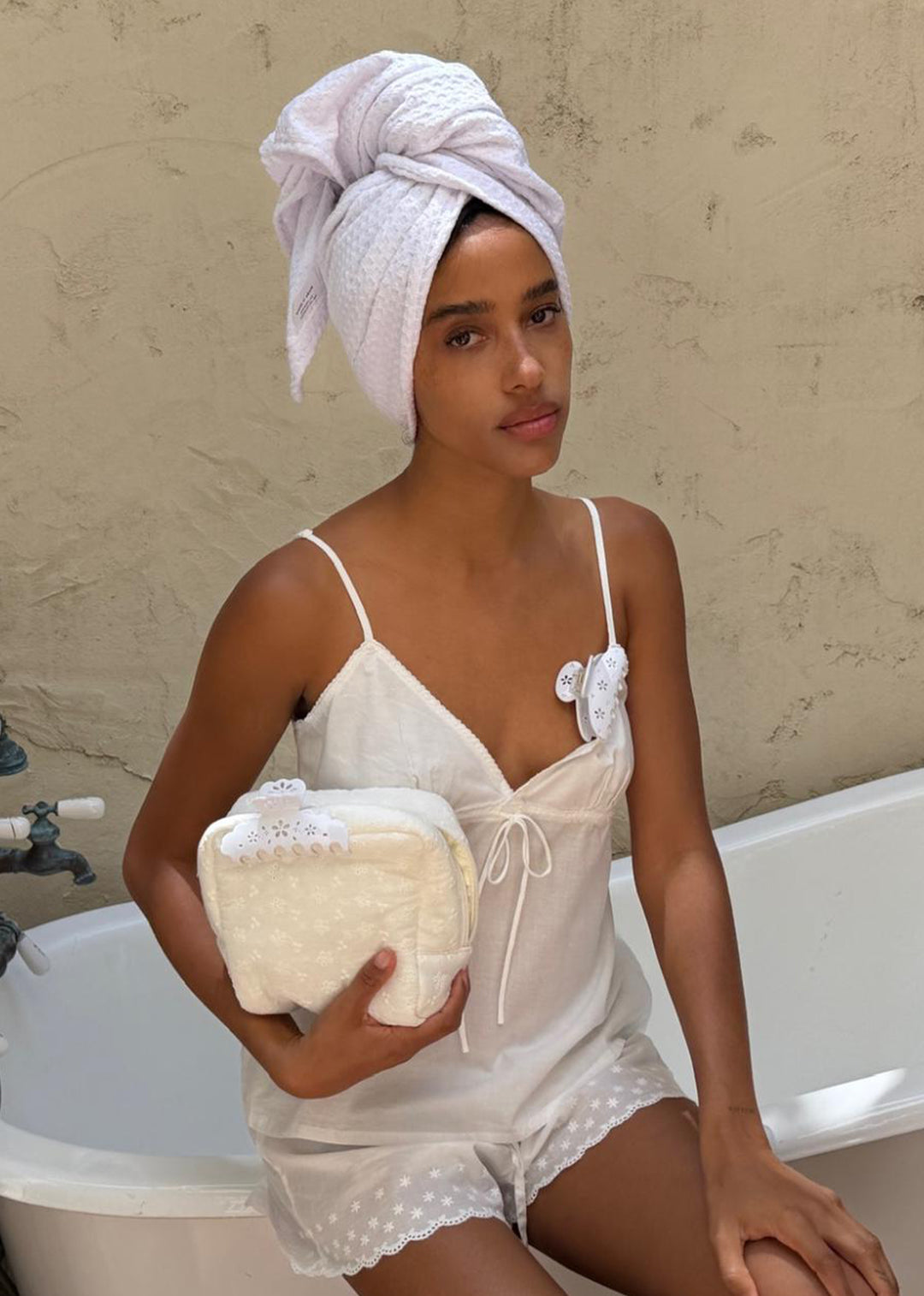 model sitting on edge of bathtub with big effing clip attached to strap of top holding dream creme