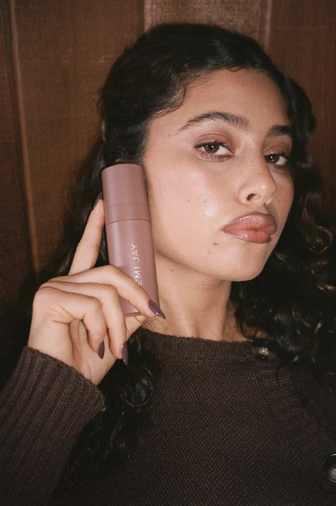 Model holding Aura Hair + Body Mist against cheek.