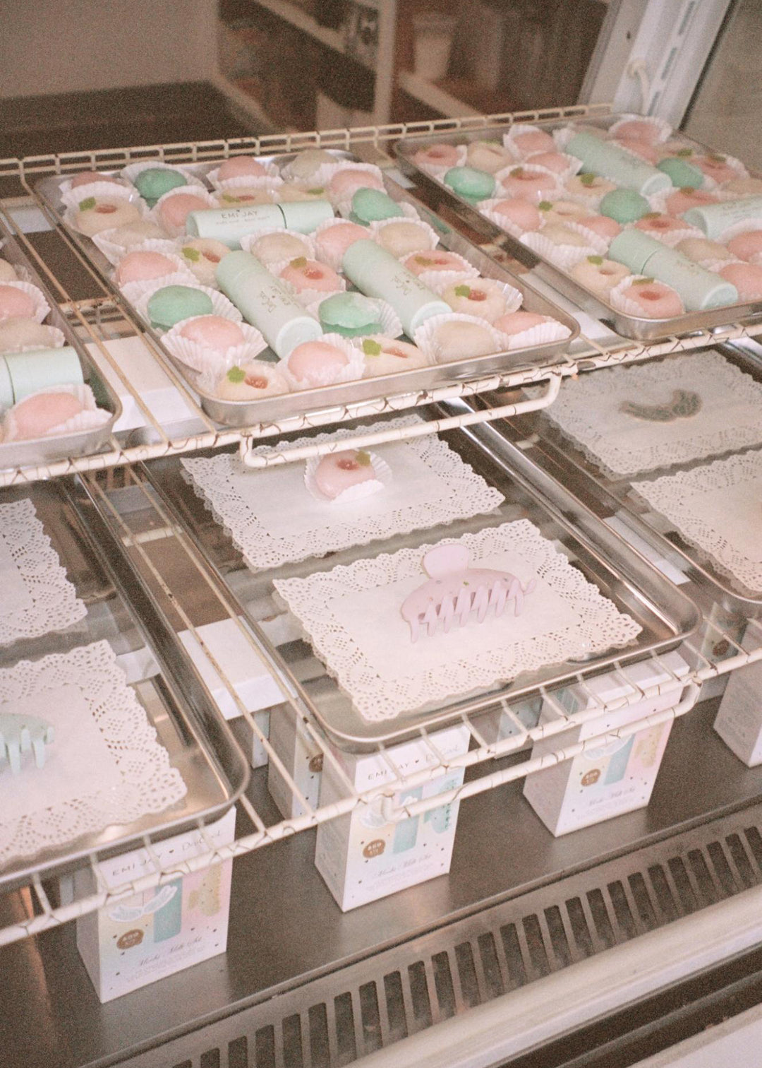 assorted dedcool x emi jay collab products with mochi treats on racks with metal trays in glass case