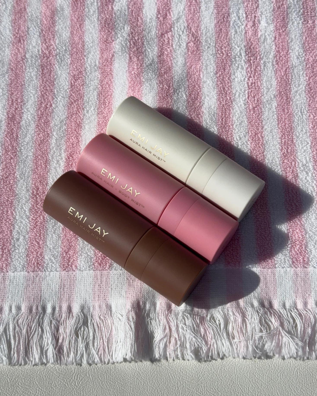 all three aura hair + body mist scents on a pink and white stripe towel