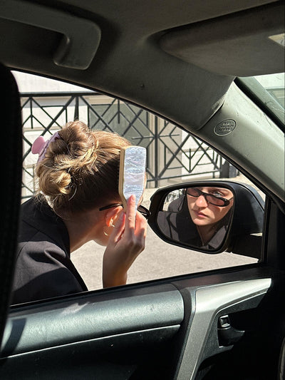 model brushing her hair with mini boar brush in side mirror of car while wearing big effing clip 