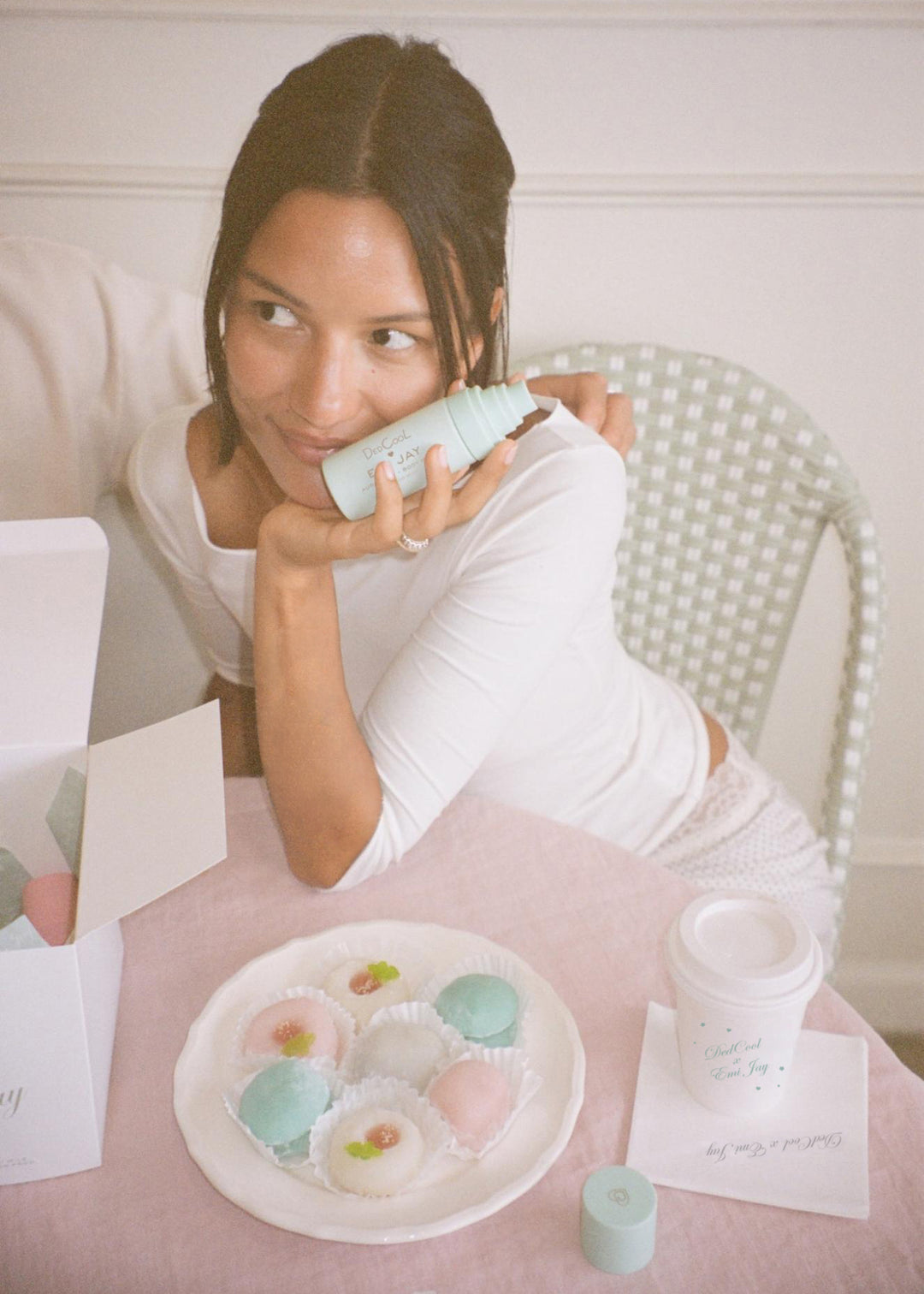 model holding aura mist while sitting at table with plate of mochi treats next to coffee on napkin