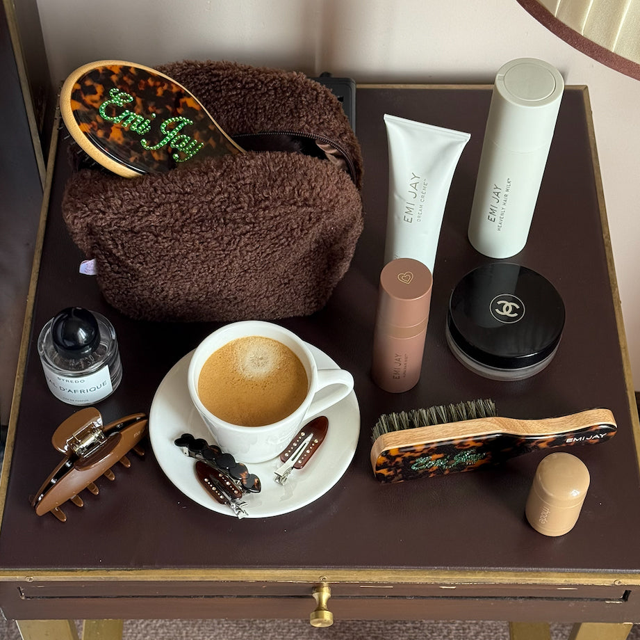 Emi Jay hair care, pouch, and accessories on table with coffee cup.