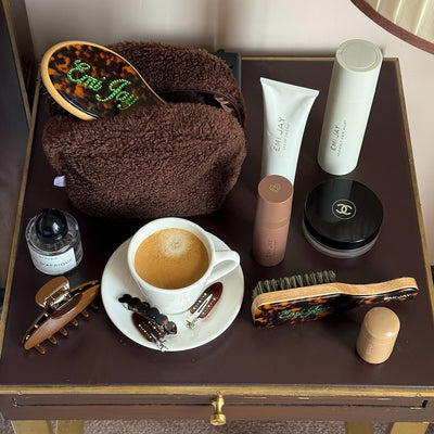 Emi Jay hair care, pouch, and accessories on table with coffee cup.