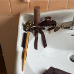 Aura Hair + Body Mist in Toasted Sugar sinkside with assorted Emi Jay hair accessories and styling tools.