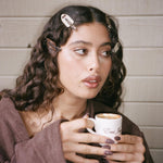 Model wearing Popstar Clips in Hazelnut Hug while holding Emi Jay mug of coffee.
