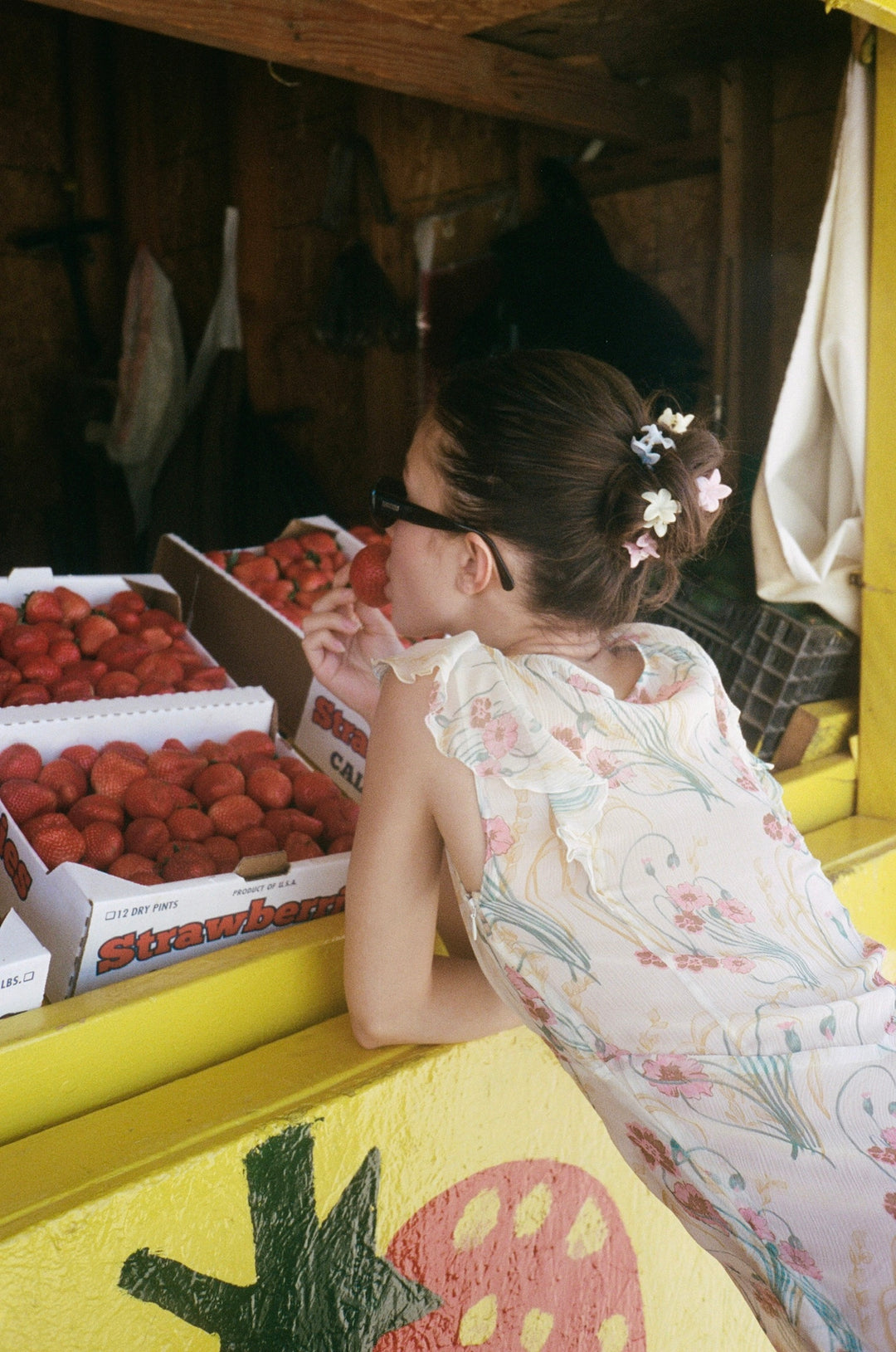 model leaning on strawberry stand with sweet like honey clips in hair