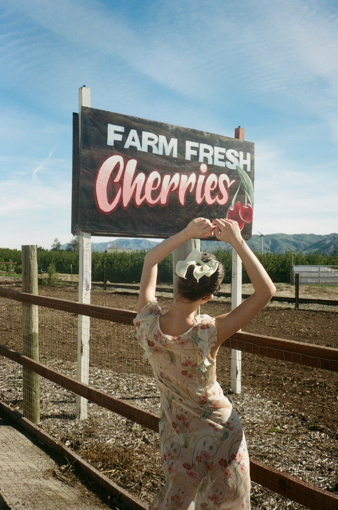 model standing in front of farm fresh cherries sign with bow barrette in hair