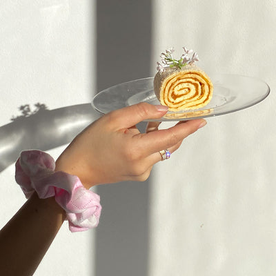 model wearing a Tie Dye Pointelle Scrunchie in Rosie on wrist while holding a plate with pastry